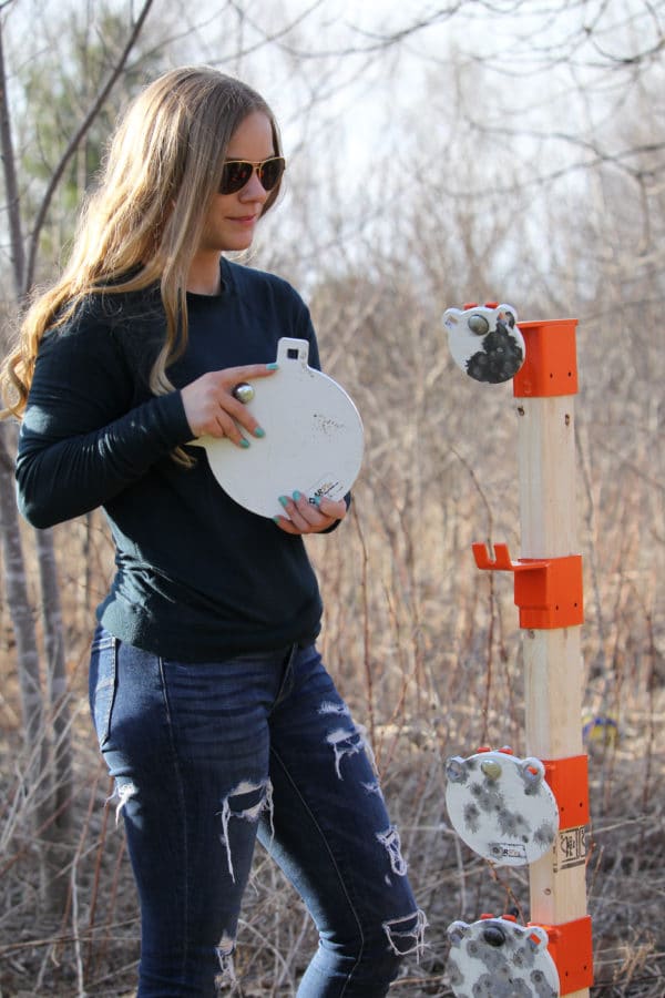 Woman in backyard setting up AR500 steel round gong targets on 2x4 mount with x-base stand